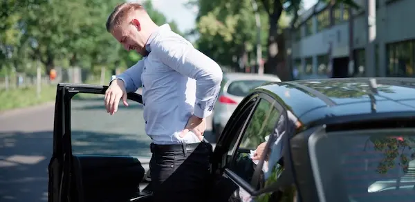 Car accident medical expenses are mounting as the injured victim experiences back pain exiting the vehicle after the collision.