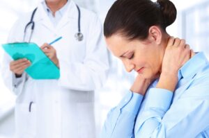 A woman in a blue shirt is holding her painful neck during a medical examination with a doctor documenting her neck injury accident symptoms in Atlanta.