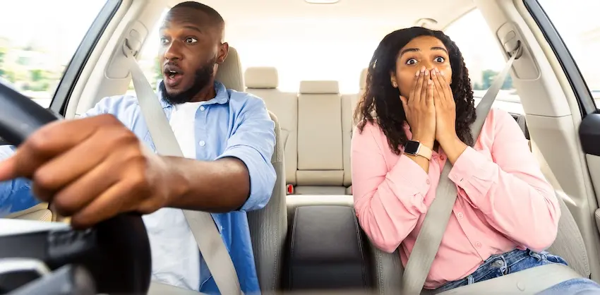 A man and woman seated inside a vehicle both react with wide-eyed shock and fear as the driver reaches toward the steering wheel capturing the terrifying moment just before impact in a Lyft accident that could leave passengers with serious injuries in Atlanta.