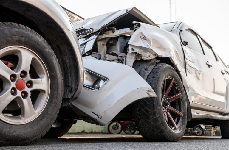 A close-up ground-level view of a silver car with its entire front end destroyed- hood peeled back- and engine components fully exposed after being crushed against another vehicle illustrating the catastrophic structural damage that results from a head-on collision in Metro Atlanta.